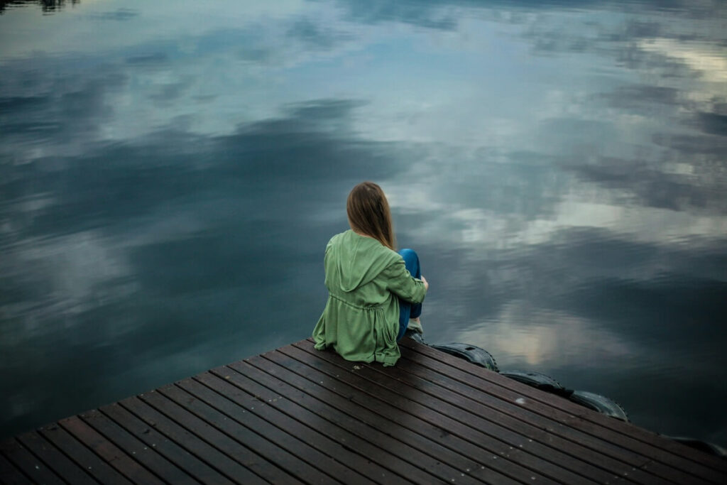 Woman gazing thoughtfully at a lake, suggesting contemplation or introspection.